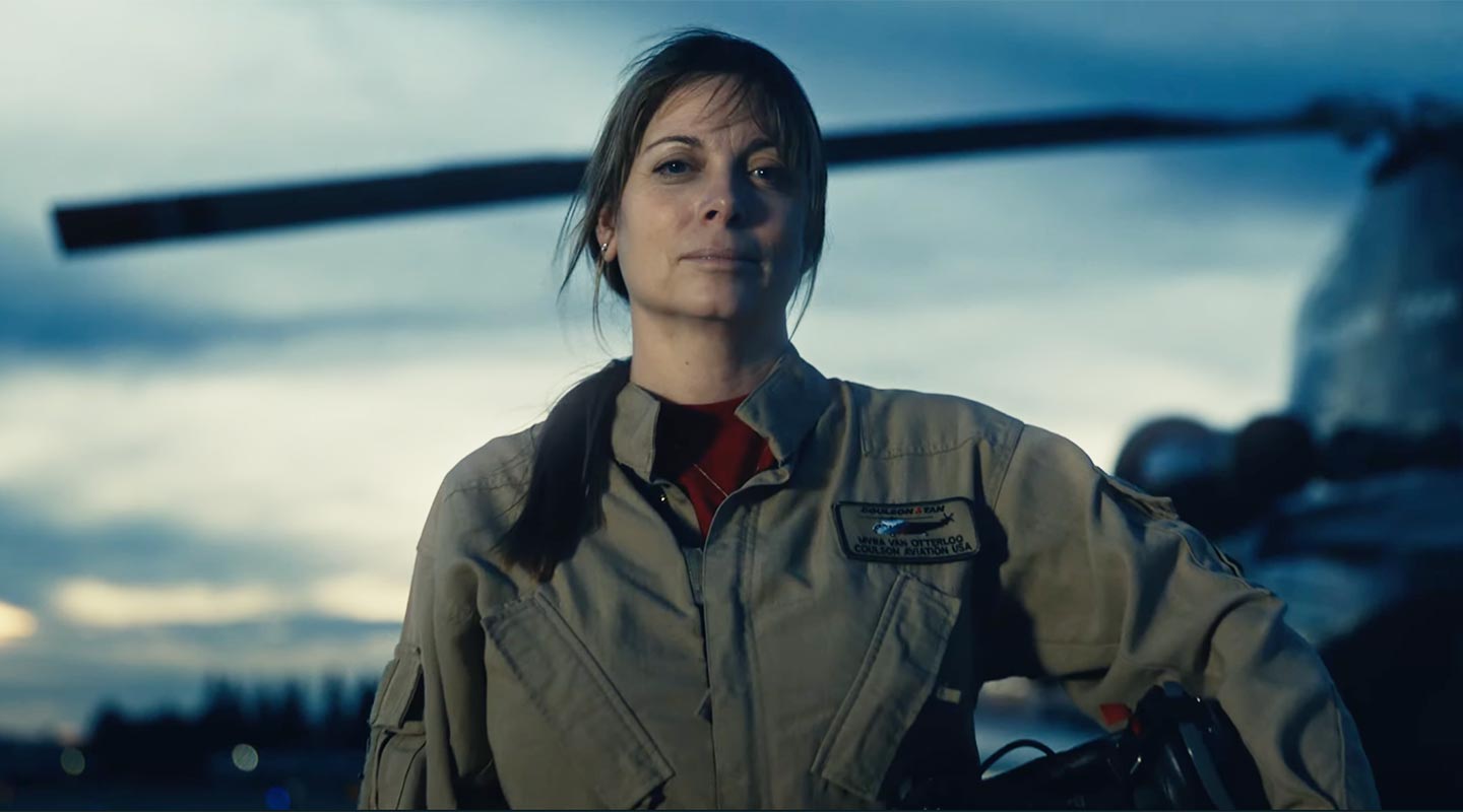 Female Caucasian pilot staring straight on with chinook helicopter in the background