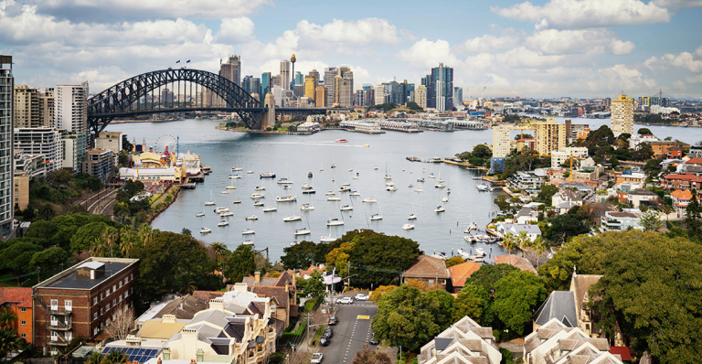 Skyline of Australia’s Syndey Harbour bridge with a cloudy blue sky.