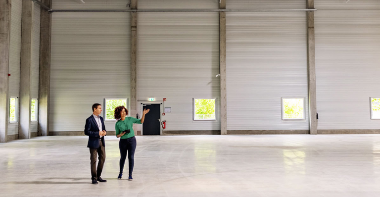 A Caucasian man and Black woman standing in an empty warehouse facility.