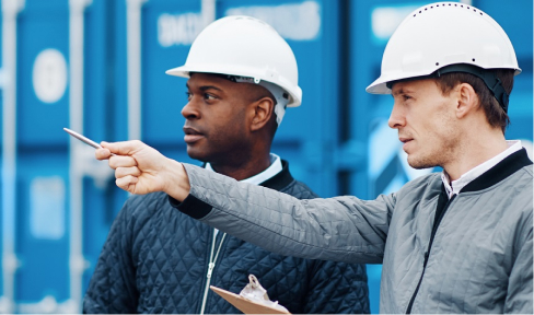 Two men in hard hats stand in front of blue shipping containers