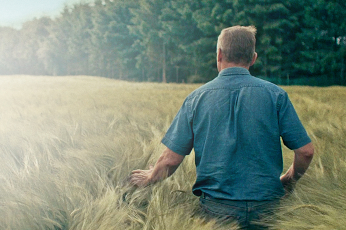 A farmer walking in the field with his back showing.