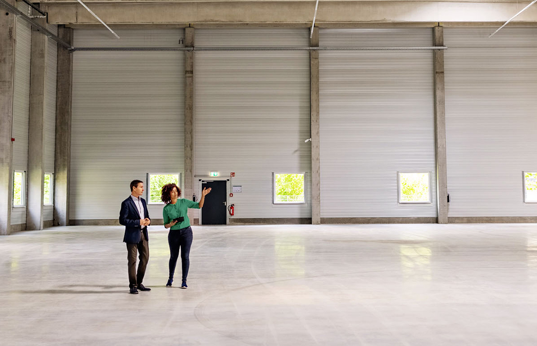 A Caucasian man and Black woman standing in an empty warehouse facility.