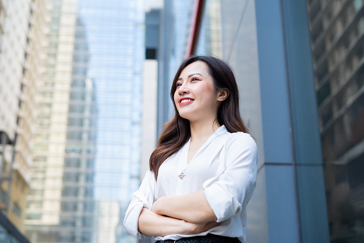 Une jeune femme asiatique se tient debout, les bras croisés, l'air confiant.